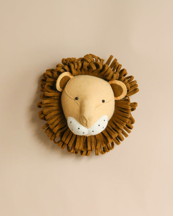 A handcrafted felt lion wall decor with a textured mane on a light beige background. The lion has a friendly face with a neutral expression and is beige with darker brown accents.