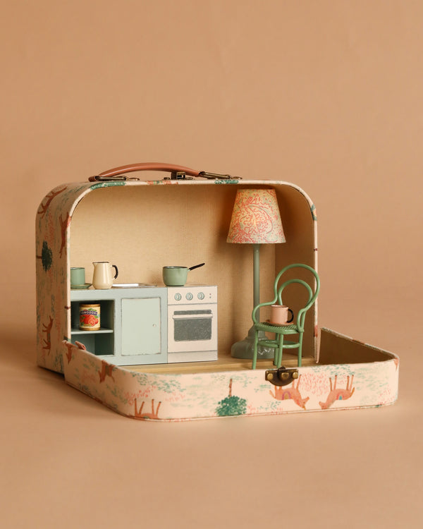 The Maileg On The Go Suitcase Set opens to reveal a miniature kitchen and dining scene, complete with a kitchen counter, pastel stove, lamp, teal vintage chair, and tiny dishes—all sized perfectly for a Maileg mouse.