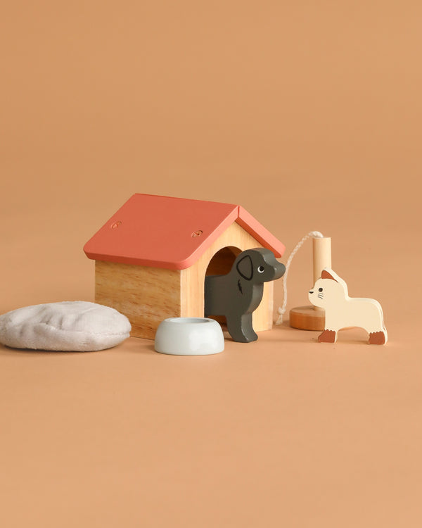 The Dolls House Pet Set features a wooden doghouse, black dog figurine, white cat on a string, gray bowl, and stone—all on a beige background. Ideal for imaginative play and small world adventures!.