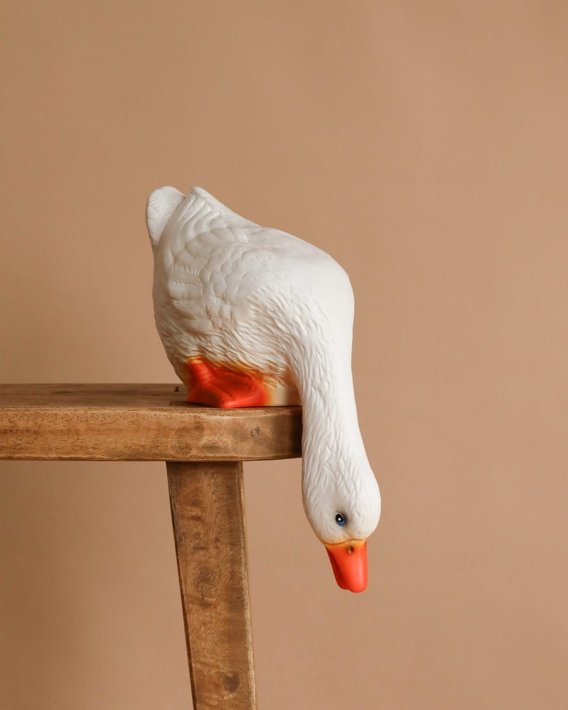 The Duck Looking Down Lamp, featuring a white duck with an orange beak and feet leaning over a wooden table edge, brings a playful accent to children's room decor against a simple beige backdrop.