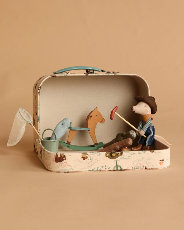 The Maileg On The Go Suitcase Set includes toy figures—a Cowboy Mouse, wooden horse, blue whale, net, stick with red ring, and green cup—beautifully arranged in a small open case against a beige background.