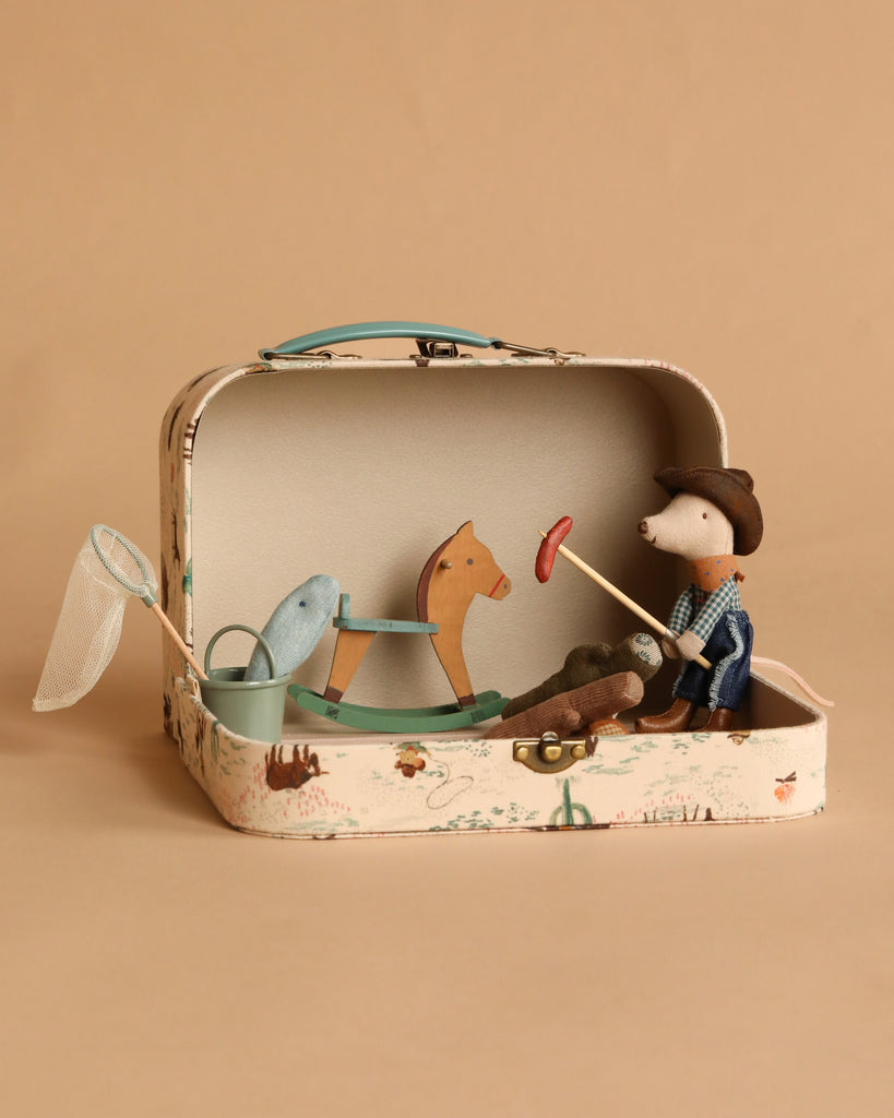 The Maileg On The Go Suitcase Set includes toy figures—a Cowboy Mouse, wooden horse, blue whale, net, stick with red ring, and green cup—beautifully arranged in a small open case against a beige background.