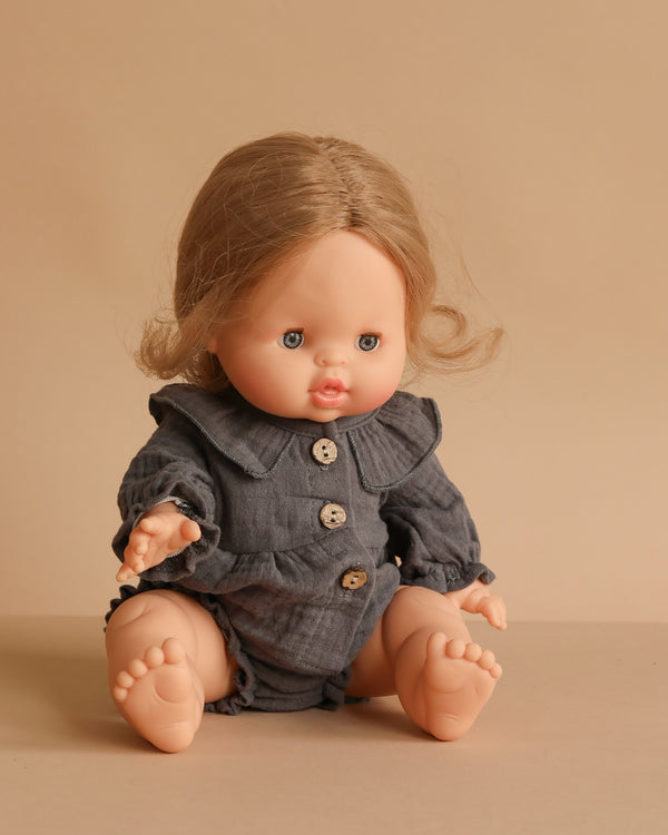 The Minikane Baby Doll (13") - Eleanor With Clothing features light skin, blue eyes, and light brown hair in a gray buttoned outfit against a beige background. Made in Spain, this anatomically correct doll is ideal for realistic play.