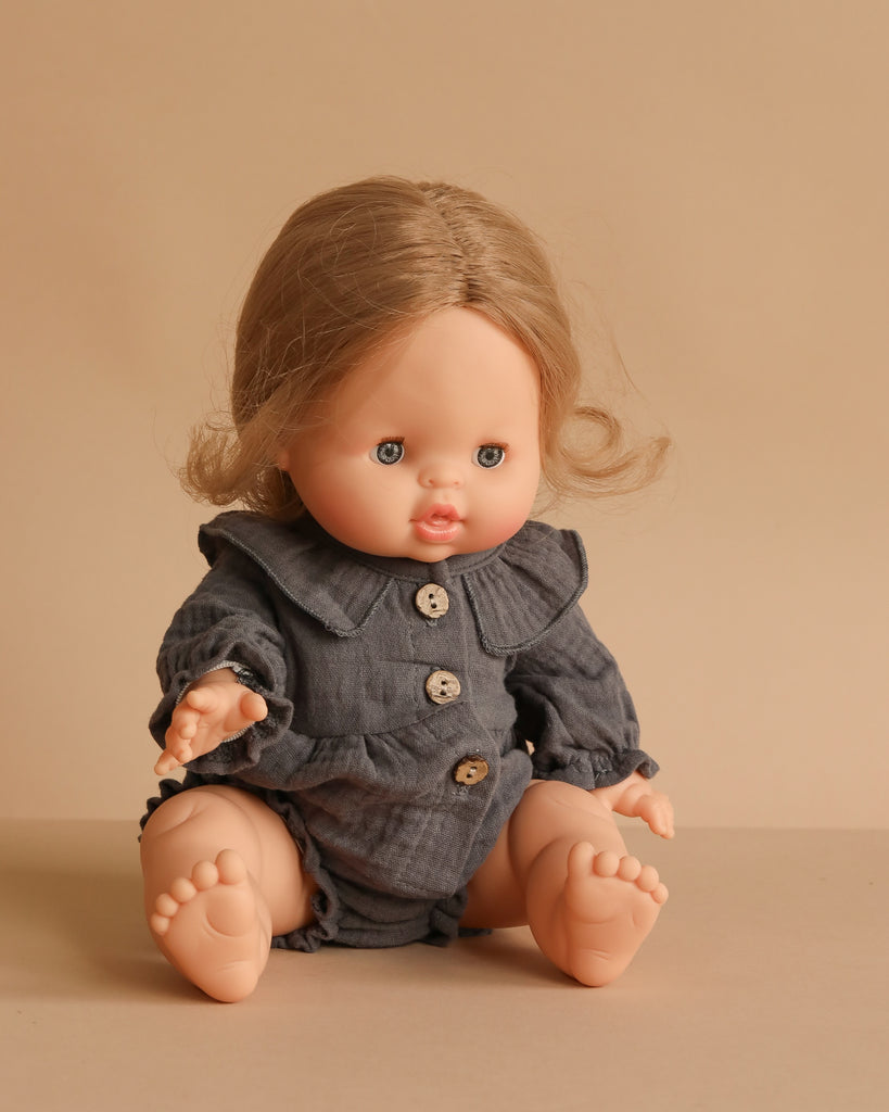 The Minikane Baby Doll (13") - Eleanor With Clothing features light skin, blue eyes, and light brown hair in a gray buttoned outfit against a beige background. Made in Spain, this anatomically correct doll is ideal for realistic play.