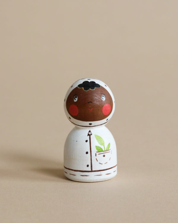 A Handmade Wooden Astronaut painted as an astronaut with dark hair, rosy cheeks, and a white space suit featuring a simple plant motif, measures 2.2" tall, set against a plain beige