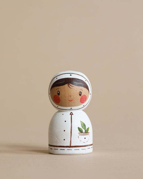A Handmade Wooden Astronaut painted to resemble a person wearing an astronaut helmet and suit, with a small potted plant motif on the suit, set against a plain beige background.