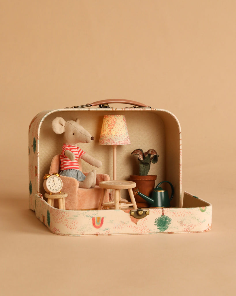 The Maileg On The Go Suitcase Set opens to reveal a cozy miniature scene: a Maileg mouse in a red striped shirt sits in an armchair, surrounded by dollhouse furniture and accessories, all against a beige background.
