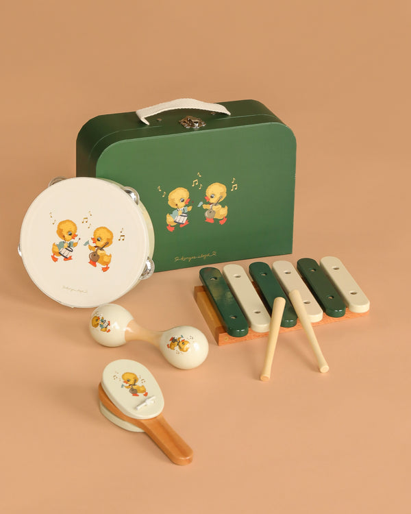 The Konges Sloejd Music Set - Green is a wooden children’s instrument set featuring a tambourine, maracas, xylophone, and castanets with yellow duckling prints, displayed on tan with a green carrying case.