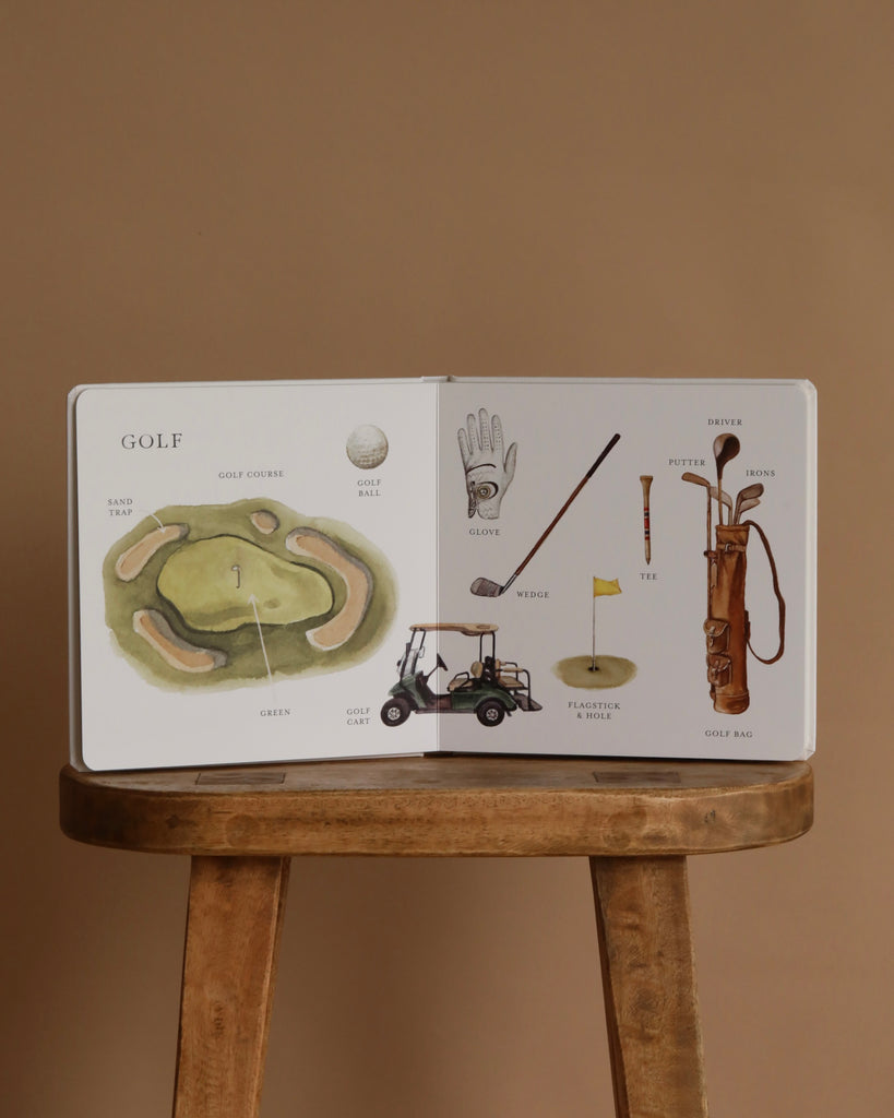 Our Big Book of Sports: A Collection of 100+ Sports Words sits open on a wooden stool, showing illustrated golf equipment and a course diagram—ideal for teaching preschool sports vocabulary. Brown background.