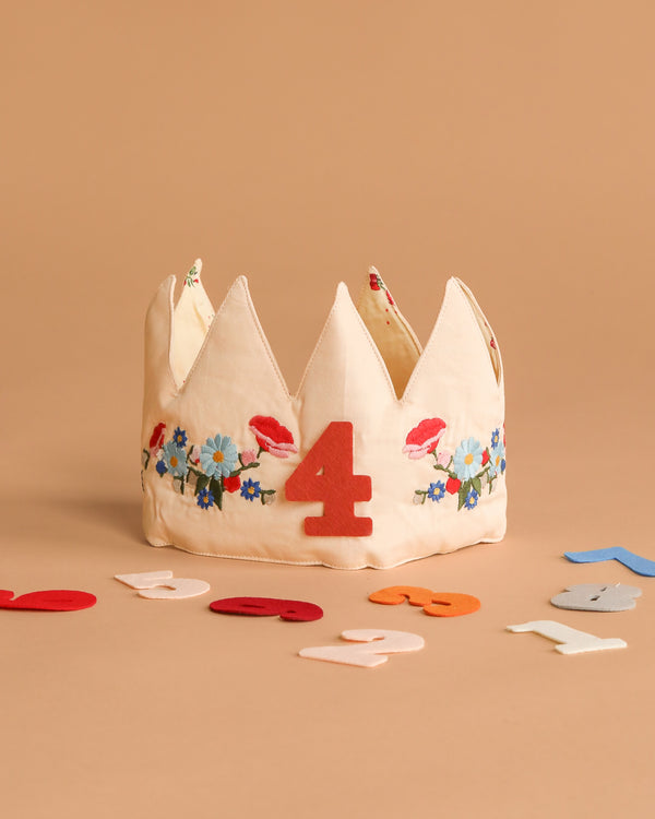 The Konges Sloejd Birthday Crown - Flower features soft fabric, embroidered flowers, and a red number 4 on the front, with colorful felt numbers displayed on a beige background.