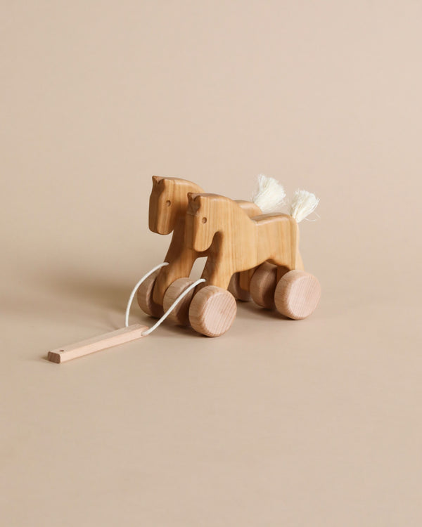 A Galloping Horses Pull Toy with wheels and a pull string, set against a plain beige background, featuring a fluffy white tail and mane.