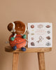 The Sports Storytime Set featuring plush football and basketball toys rests on a wooden stool beside an illustrated preschool sports book, all set against a beige background.