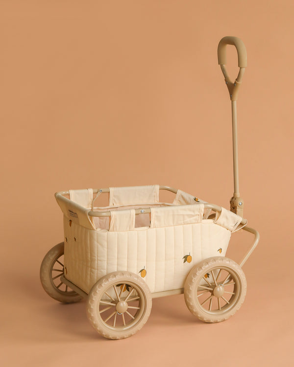 The Konges Sloejd Stroller Kids Wagon - Lemon is a beige stroller wagon with quilted fabric sides, small yellow lemon motifs, four large wheels, and a tall curved handle—shown on a matching beige background.
