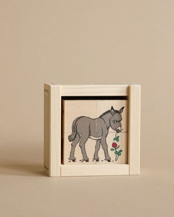 A small wooden box with a sliding lid, crafted from sustainably harvested trees, displaying a black ink illustration of a Wooden Block Puzzle - 4 Piece Farm Animals, set against a pale beige background.