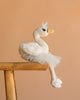 The Bukowski - Odette Ballerina Swan - White plush features a tutu and ballet shoes, elegantly posed on a wooden stool against a plain beige background.