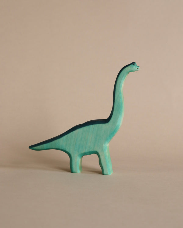 A blue Handmade Holzwald Brachiosaurus toy stands on a plain beige background. Its neck is elongated and it looks to the right. This model is part of our educational collection.