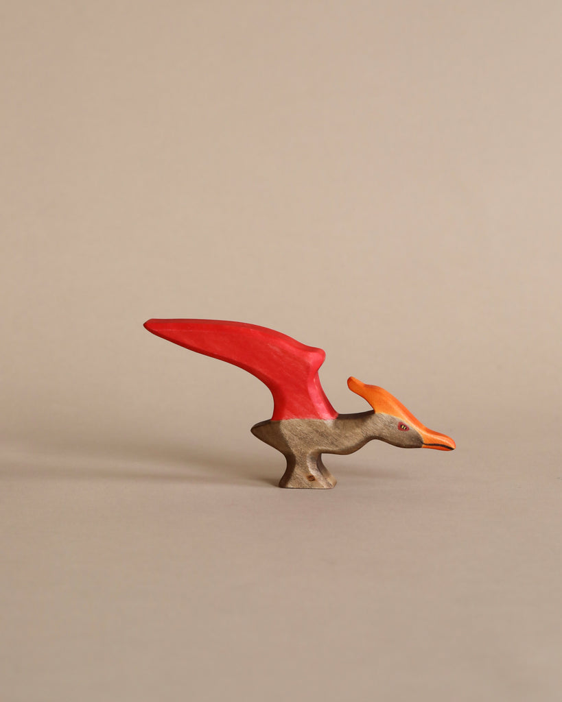 A small sustainable Handmade Holzwald Pteranodon with a bright red crest and beak, positioned upright against a plain, light beige background.