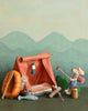 The Maileg Bonfire set features a small toy tent with a hanging lantern, surrounded by gear like a life preserver, paddle, fishing rod, and net. A hiking mouse figurine with a walking stick stands nearby against painted mountain scenery.