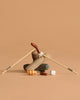 Two chopsticks form an upside-down V over log-shaped fabric, a plush croissant, and marshmallows—this whimsical Maileg Bonfire set inspires imaginative camping adventures, displayed on a plain beige background.