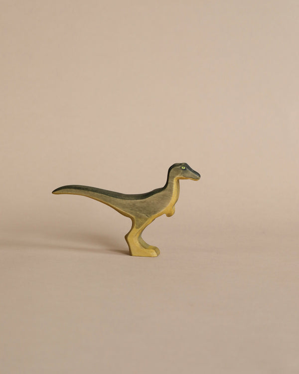 A high-quality Handmade Holzwald Velociraptor toy, resembling a velociraptor, stands on a plain beige background. The toy is painted with shades of yellow and green.