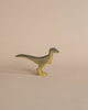A high-quality Handmade Holzwald Velociraptor toy, resembling a velociraptor, stands on a plain beige background. The toy is painted with shades of yellow and green.