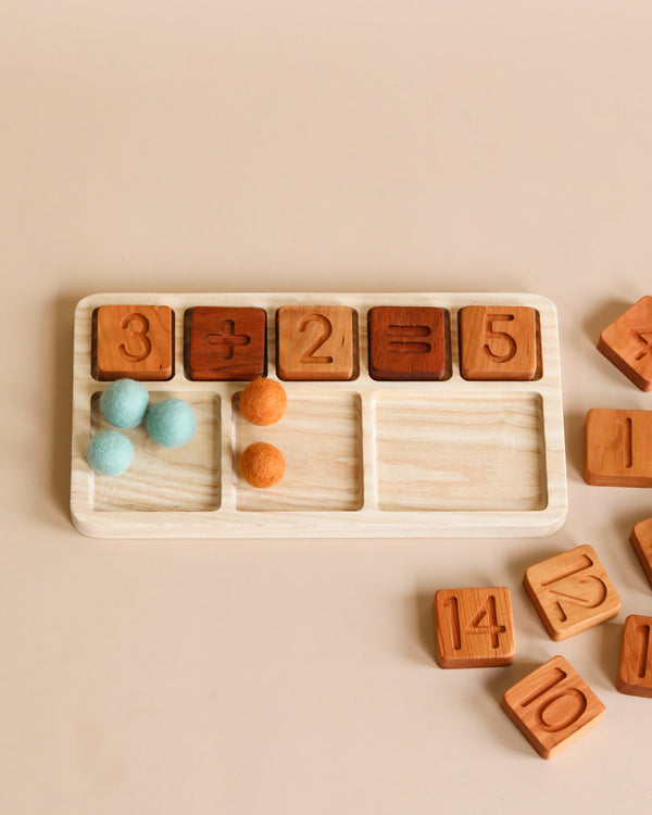 A The Original Wooden Math Board - Made in USA, featuring a wooden tray with compartments holding wooden blocks numbered 3, 2, 5, and colorful felt balls on a soft beige background. Additional number blocks scattered