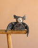 Bukowski - Ziggy Bat, a gray Halloween plush with soft velvet wings and pointed ears, sits on a wooden stool against a plain beige background.