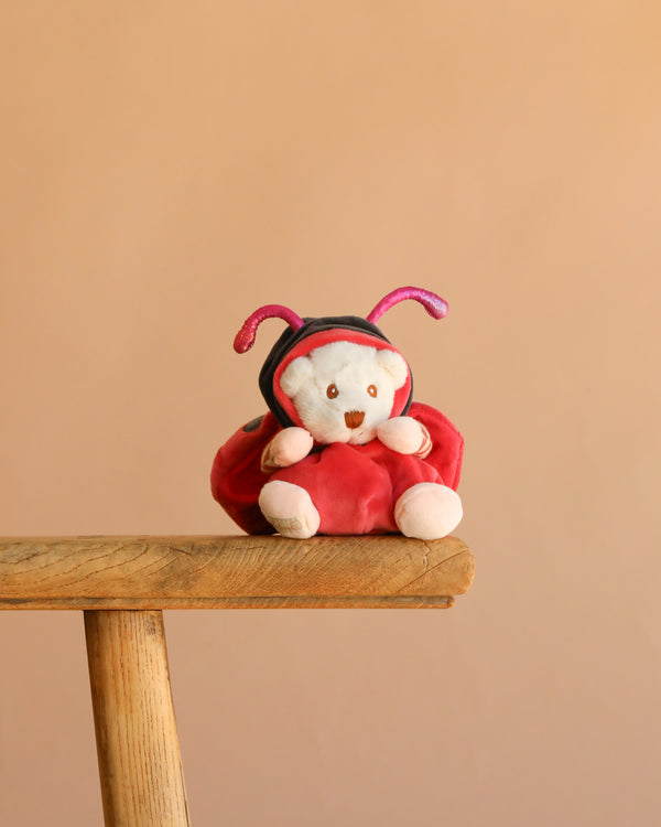 The Bukowski - Ziggy Ladybug plush bear, dressed in a red and black ladybug costume, sits on a wooden stool with a plain beige background.