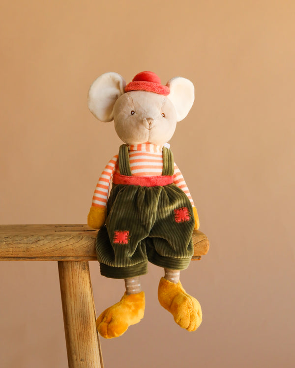 Bukowski - Henry Mouse is a baby-safe stuffed animal wearing a red hat, orange and white striped shirt, green corduroy overalls with red patches, and yellow shoes, seated on a wooden stool against a beige background.