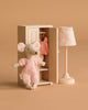 A Maileg Springtime Wardrobe Set features a small beach mouse in pink overalls beside a mouse closet filled with pink clothes and a cream vintage floor lamp with a floral shade, all set against a beige background.