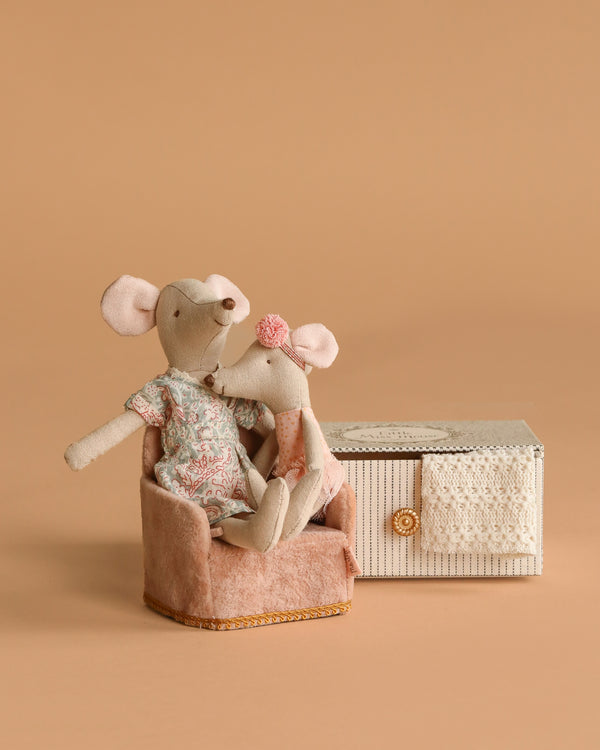 The Maileg Mommy and Me Set features two fabric toy mice seated on a soft pink folding chair beside a small lace-trimmed decorative box, all displayed against a plain beige background.