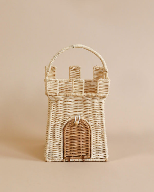 A handwoven Olli Ella | Rattan Castle Bag shaped like a castle with a central arched doorway and cylindrical towers, set against a plain beige background.