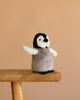The Steiff Flaps Penguin, a small plush toy with outstretched wings, stands on a wooden stool against a plain beige background—an adorable heirloom piece for any collection.