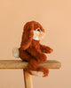 The Steiff Bommel Dangling Rabbit, a brown and white bunny plush with floppy ears, sits on a wooden stool against a beige background—ready to be your perfect snuggle buddy.