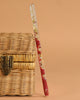 The Konges Sloejd Magical Glitter Wand - Cherry, decorated with red and gold floral designs, leans gracefully against a closed wicker basket with a metal latch on a simple beige background.
