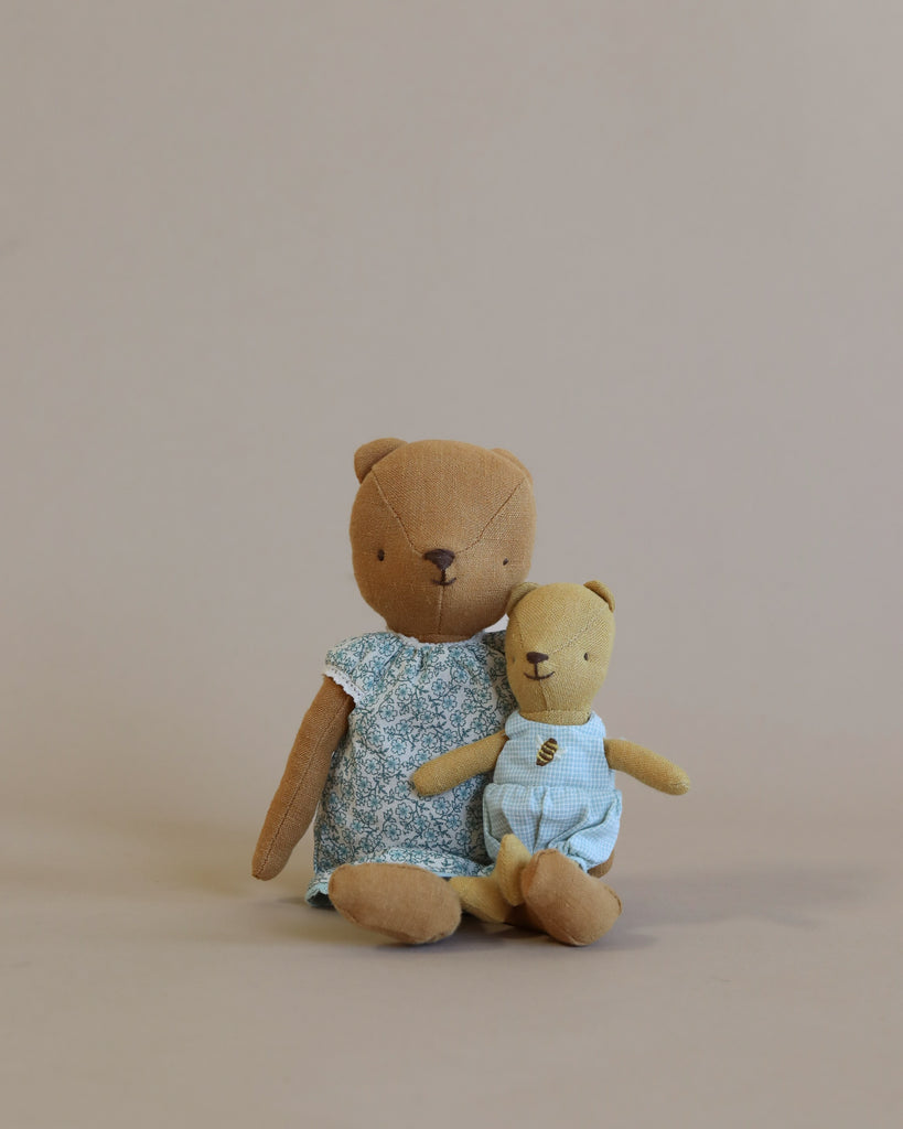 Two Maileg Teddy Mom & Baby Sets, one larger wearing a floral dress and one smaller in a striped outfit, sitting together against a plain beige background.