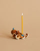 A whimsical Octopus Cake Topper shaped like an octopus, hand painted and crafted from fine porcelain, with a lit yellow candle standing upright from its center, against a soft beige background.