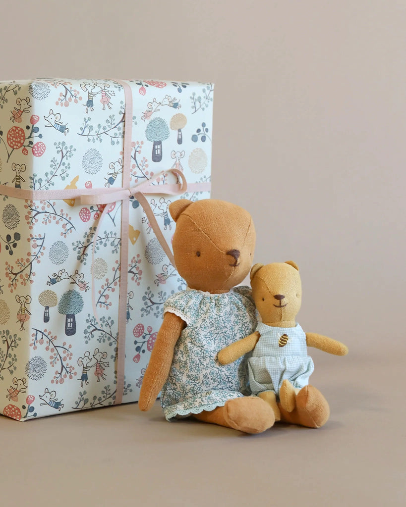 Two plush teddy bears, one large Maileg Teddy Mom in a floral dress and one small in a striped suit, sit in front of a decorative gift-wrapped box with a floral and lantern