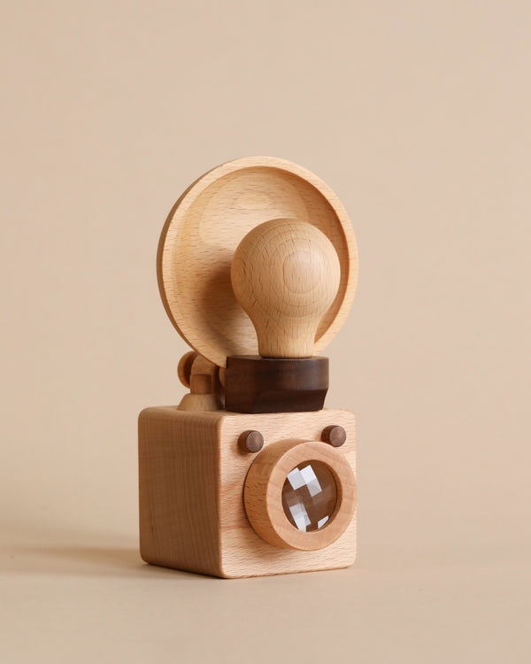 A Father’s Factory | Wooden Light Bulb Camera rubber stamp with a handle, mounted on a block with a reflective glass lens, set against a beige background.