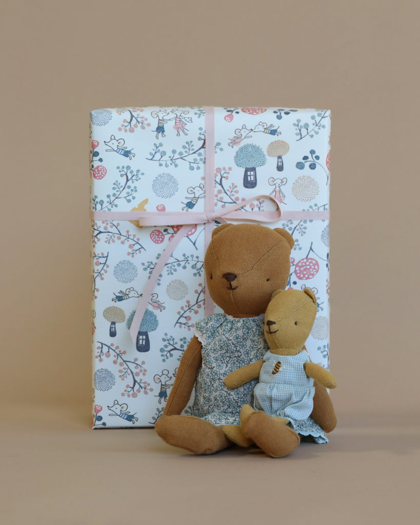 A Maileg Teddy Mom & Baby Set - Gift Wrapped sitting in front of a large gift wrapped box in floral pattern paper, set against a beige background.