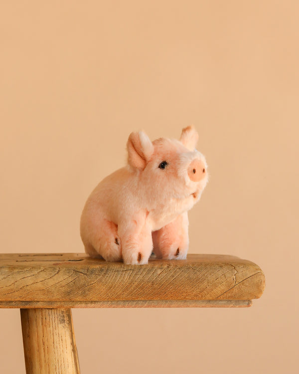 The Steiff Sissi Piglet, a small pink plush toy, is displayed on a rustic wooden stool with a plain beige background.