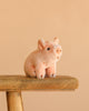 The Steiff Sissi Piglet, a small pink plush toy, is displayed on a rustic wooden stool with a plain beige background.