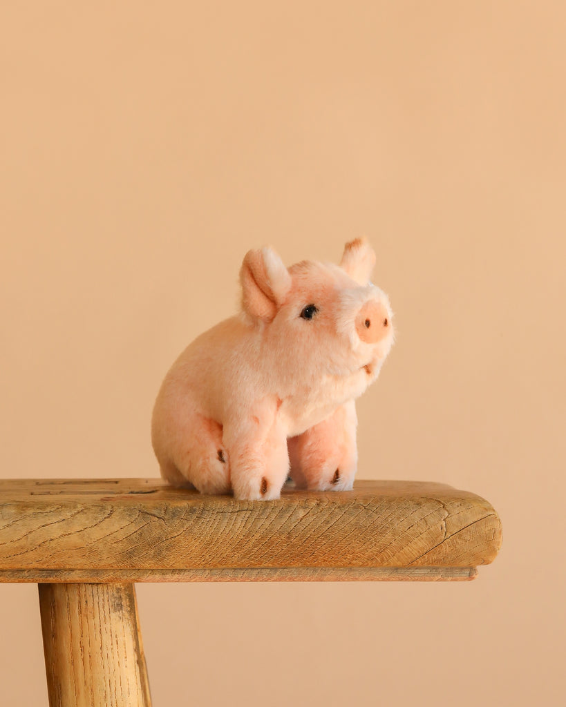 The Steiff Sissi Piglet, a small pink plush toy, is displayed on a rustic wooden stool with a plain beige background.
