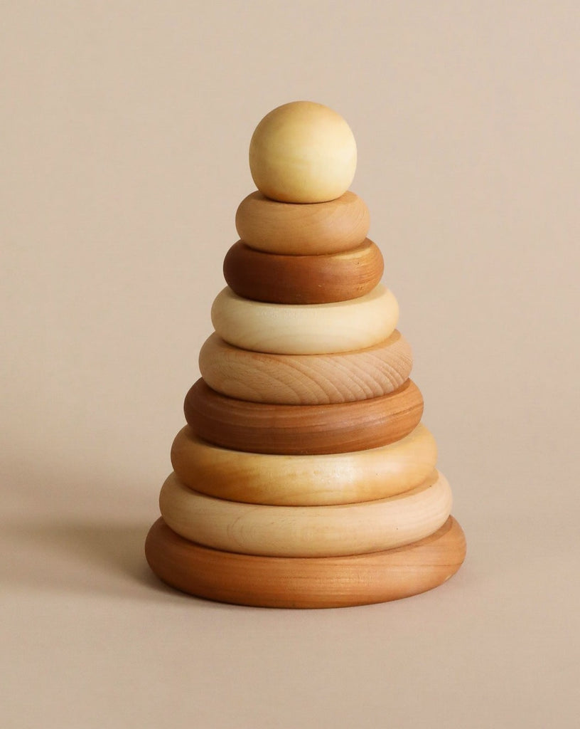 A wooden stacking toy with wooden rings in various natural shade of wood, stacked from large to small, topped with a sphere shaped wooden piece. 