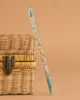 A Konges Sloejd Magical Glitter Wand - Green Mix leans against a closed woven wicker chest with a metal latch, set against a beige background.