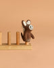 The Felt Finger Puppet: Donkey, Brown is a small, handmade puppet with a happy expression, crafted from needle-felted wool in Nepal and displayed upright on a light wooden stand against a beige background.