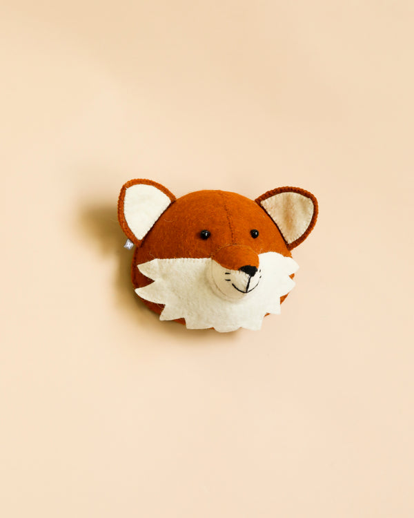 A handcrafted felt baby fox wall decoration with embroidered features on a soft beige background, made from organic wool. The fox features prominent ears, a mane, and a cute nose.