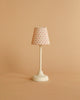 The Maileg Little Brother and Sister Bedroom Set features a small white table lamp with a round base and a red polka dot fabric lampshade, perfect for adding charm to any Maileg dollhouse. Shown on a plain beige background.