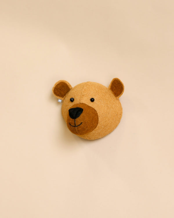 A handcrafted felt bear cub wall decor with a friendly smile on a plain beige background. The bear appears soft with prominent ears and a simple, happy expression.