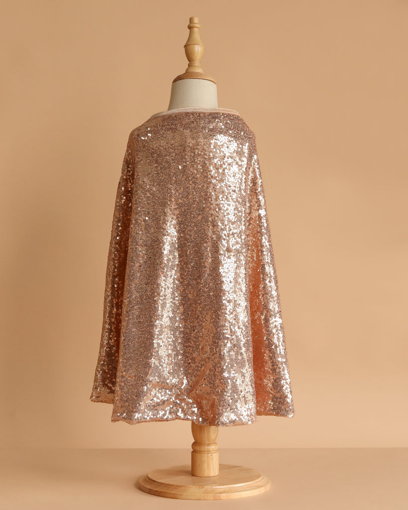 A child-sized mannequin showcases the Cape - Pink sequins against a plain beige background, with the sparkling pink costume draping elegantly from shoulders to mid-calf.